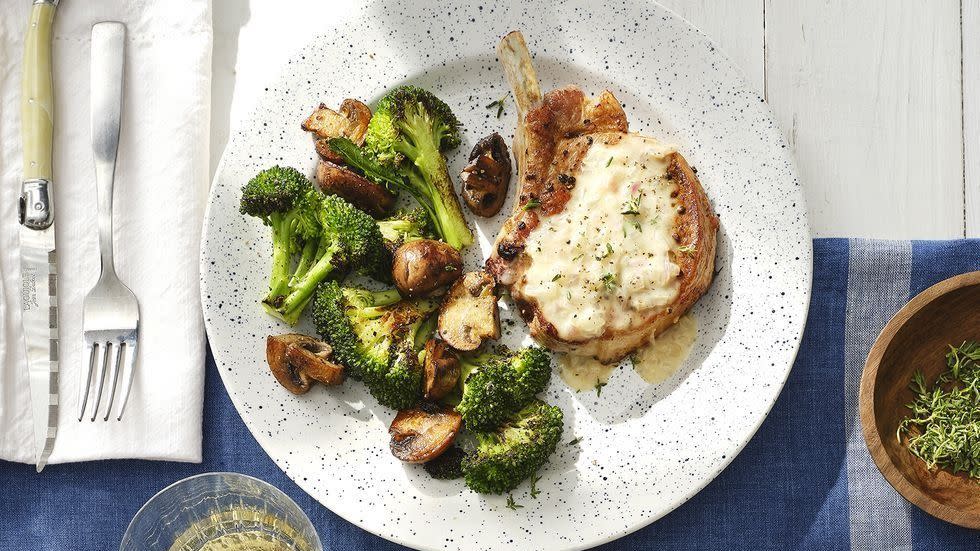 smothered pork chops with broccoli and mushrooms on a white speckled plate with a fork