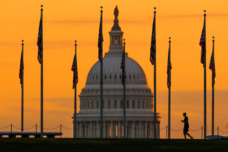 An early morning pedestrian is silhouetted against sunrise as he walks through the U.S. Flags on the National Mall and past the Capitol Building in Washington, on Nov. 7, 2022, one day before the midterm election will determine the balance of power in Congress.