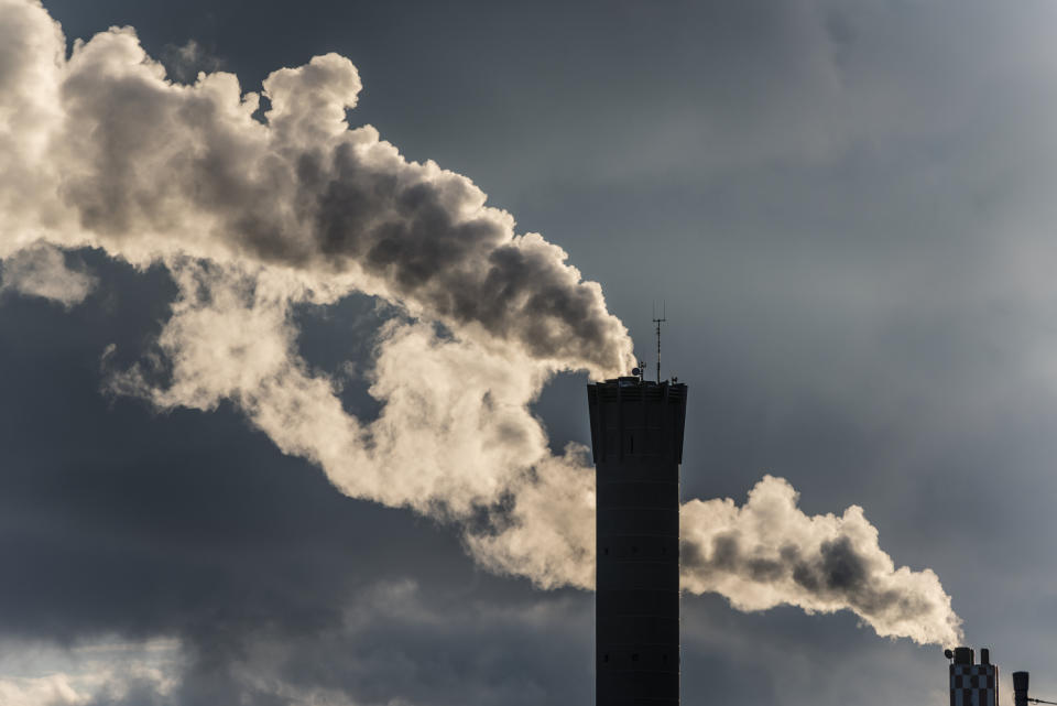 Industrial smokestacks emitting plumes of smoke against a cloudy sky