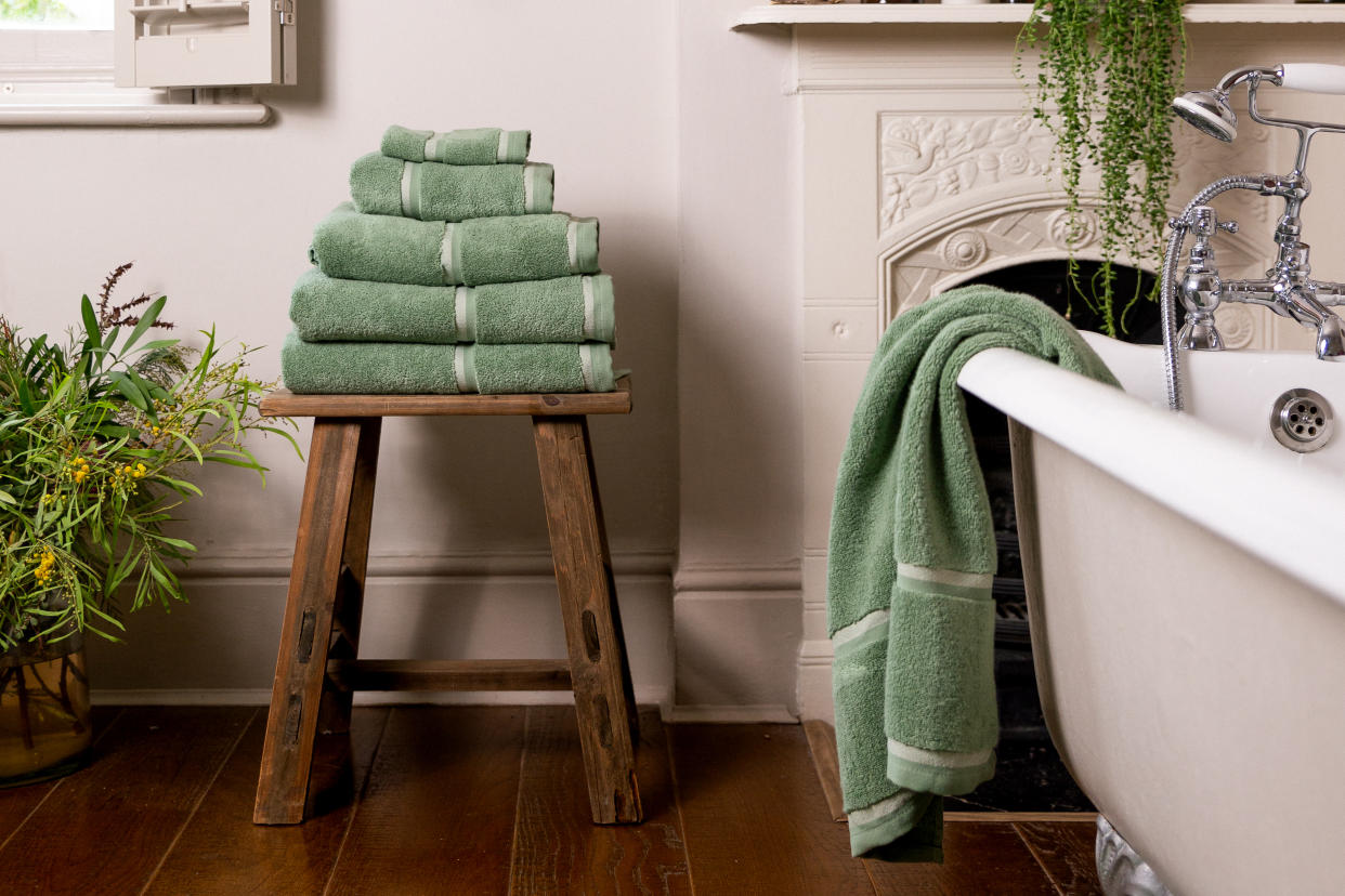  A bathroom with a white fireplace and a stack of sage green towels on a wooden stool. 