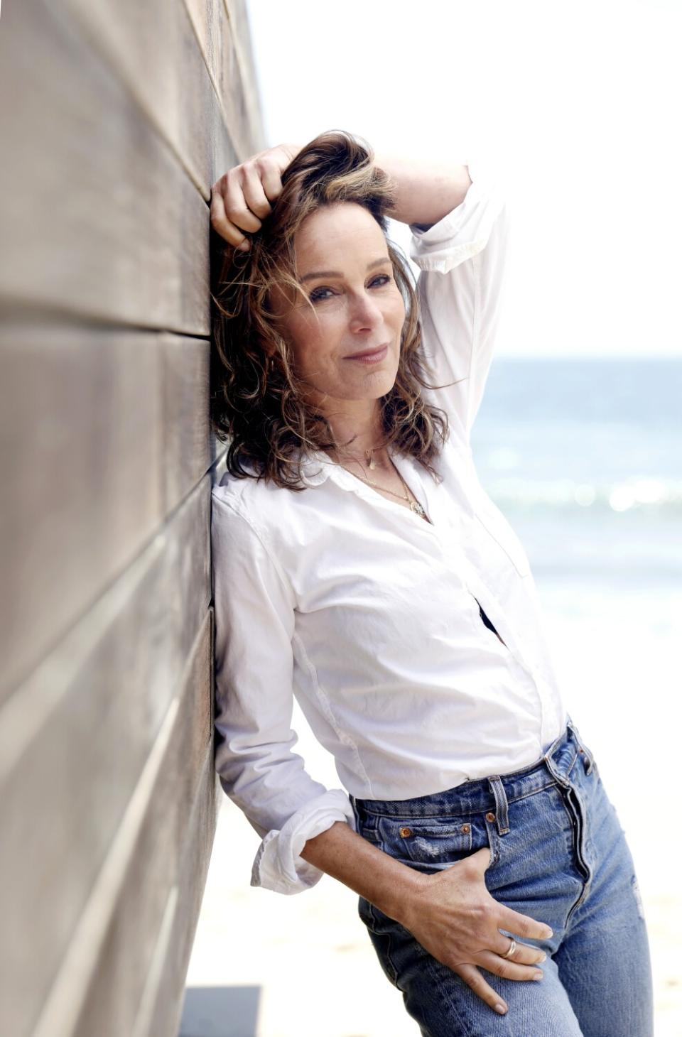 A woman in a white shirt and blue jeans leans against a wall