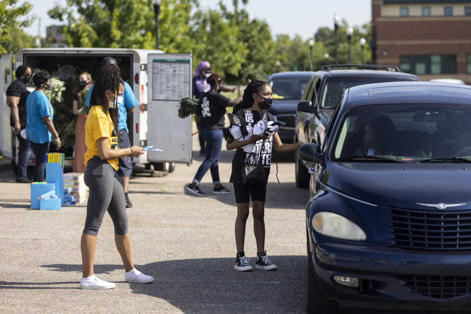 Volunteers Paris Wilkerson, left, and Makhayla DesRosiers, right, distribute Black Voters Matter fans, shirts and wristbands as other volunteers distribute groceries Saturday, May 8, 2021, at Carver High School in Montgomery, Ala. The care packages were part of the program in the John Lewis Advancement Act Day of Action. (AP Photo/Vasha Hunt)