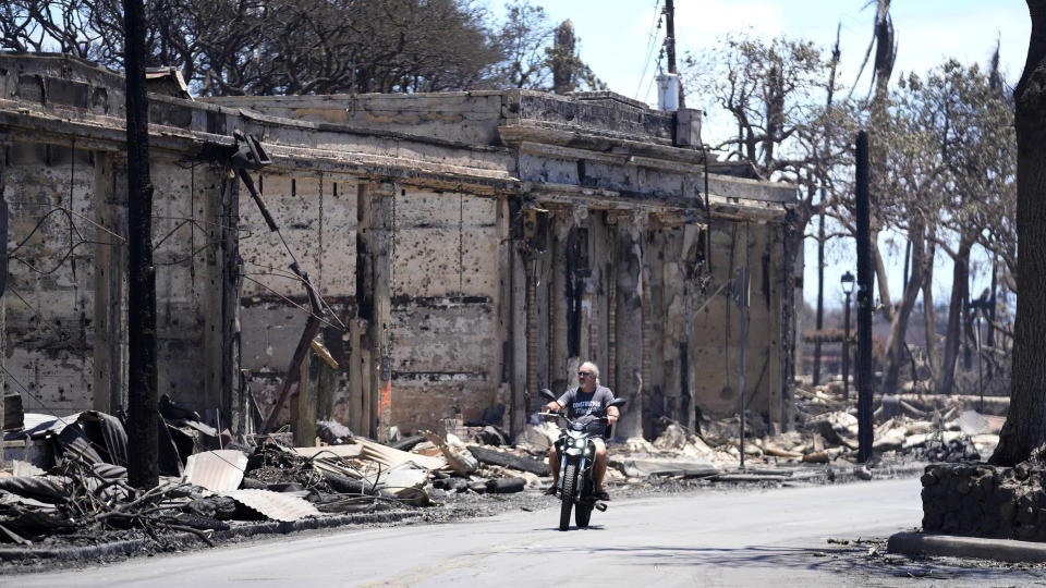 A man rides amid damage caused by wildfire, Friday, Aug. 11, 2023, in Lahaina, Hawaii. (AP Photo/Rick Bowmer)