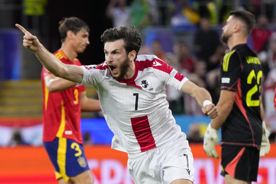 Georgia's Khvicha Kvaratskhelia celebrates after Spain's Robin Le Normand, left, scored an own goal past Spain's goalkeeper Unai Simon, right, during a round of sixteen match between Spain and Georgia at the Euro 2024 soccer tournament in Cologne, Germany, Sunday, June 30, 2024. (AP Photo/Manu Fernandez)