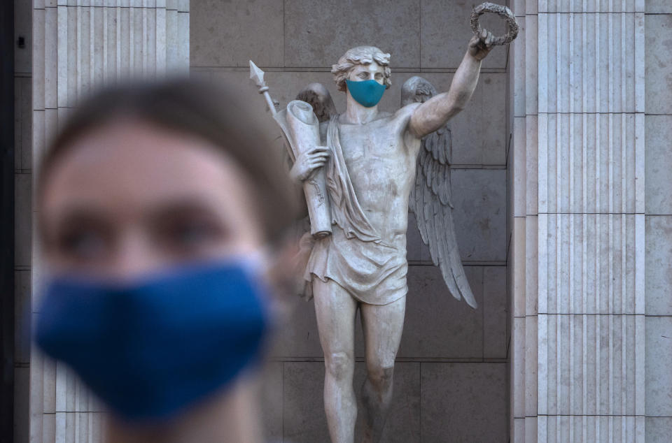 A woman wearing a face mask to protect against coronavirus infection walks past a statue with a face mask at a mall in St. Petersburg, Russia, Monday, Sept. 14, 2020. Russia has seen an increase in new cases of coronavirus in recent weeks and hospitalizations have started to increase. (AP Photo/Dmitri Lovetsky)