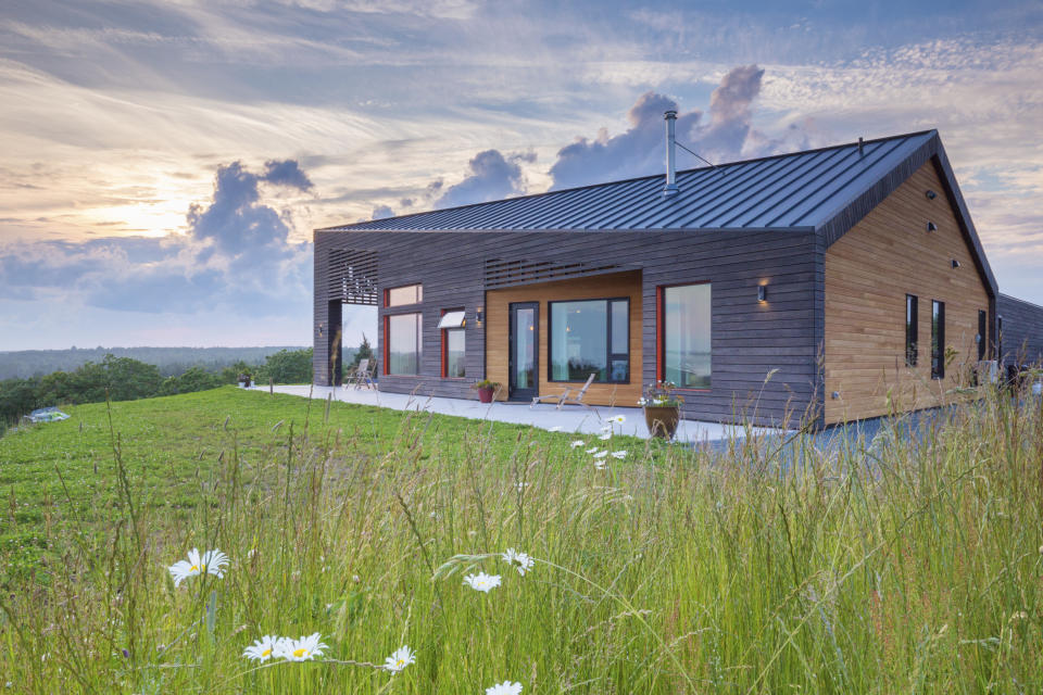 This photo provided by Adam Cornick/Taunton Press shows a photo of a home in Cow Bay, Nova Scotia, Canada, featured in the book "downsize: Living large in a small house," by Sheri Koones. The gable roof rises higher in the more public spaces to take advantage of the view with larger windows and is lower in the smaller-windowed bedroom area. The materials are low maintenance, including the standing-seam aluminum roof, locally harvested and manufactured Shou Sugi Ban wood, and spruce shiplap siding. Orange trim around the windows adds a warm pop of color. (Adam Cornick, Acorn Art & Photography/Taunton Press via AP)