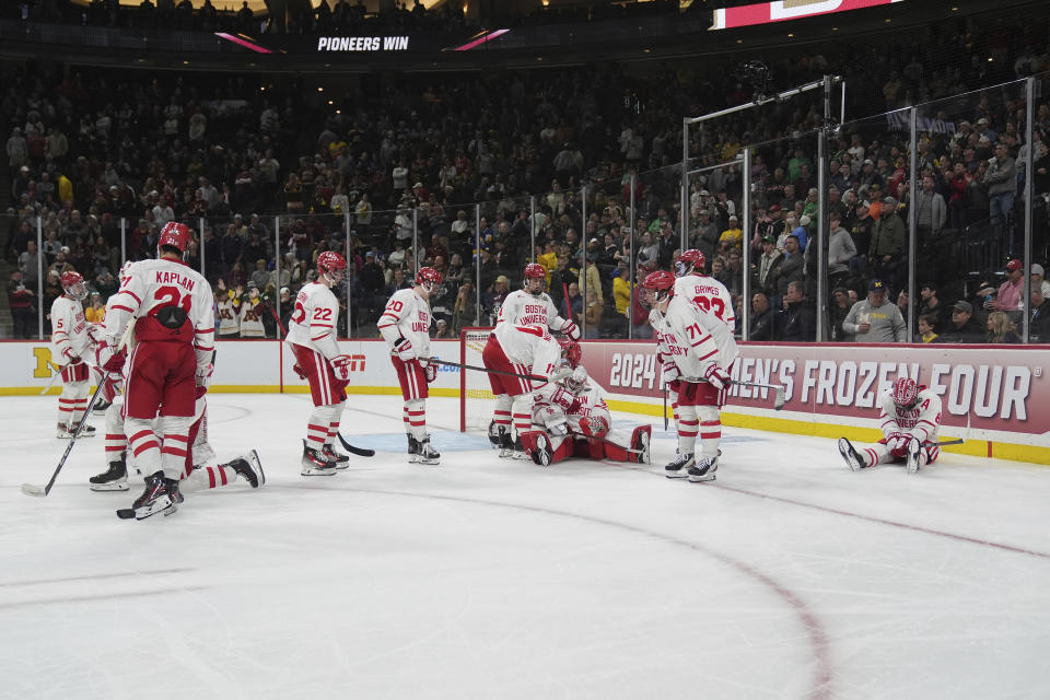 Boston University players sit and stand on the ice after an overtime loss to Denver in a semifinal game at the Frozen Four NCAA college hockey tournament Thursday, April 11, 2024, in St. Paul, Minn. (AP Photo/Abbie Parr)