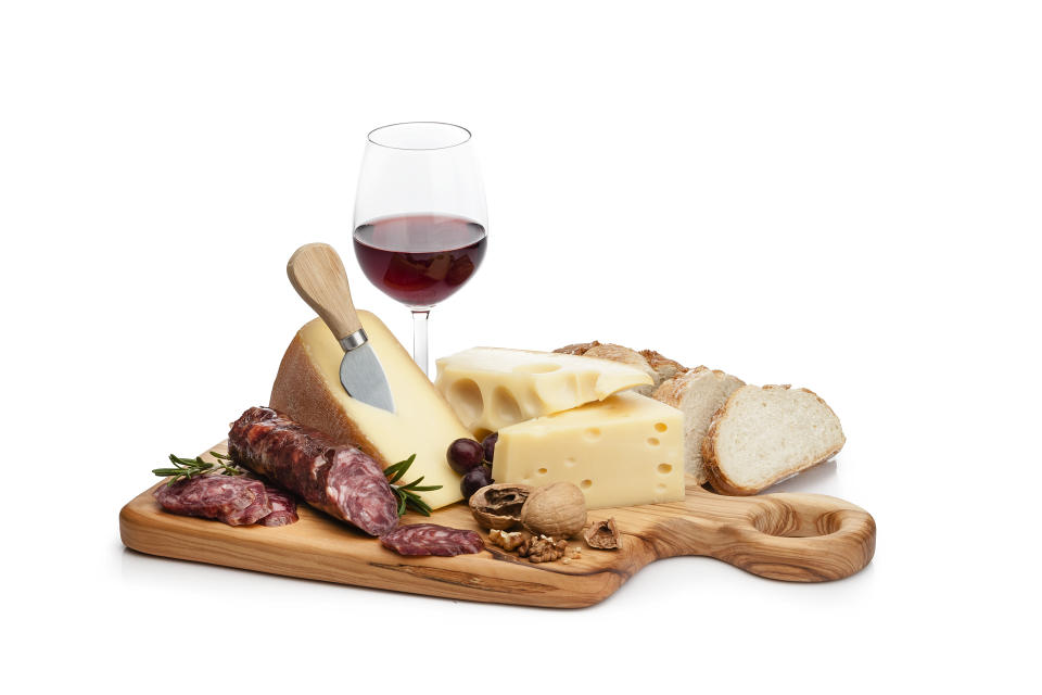 Cheese and wine: cutting board with cheese slices, spanish chorizo, grape and walnuts isolated on white background. A red wine bottle and a wineglass are behind the cheese tray. Useful copy space available for text and/or logo. High key DSRL studio photo taken with Canon EOS 5D Mk II and Canon EF 100mm f/2.8L Macro IS USM.