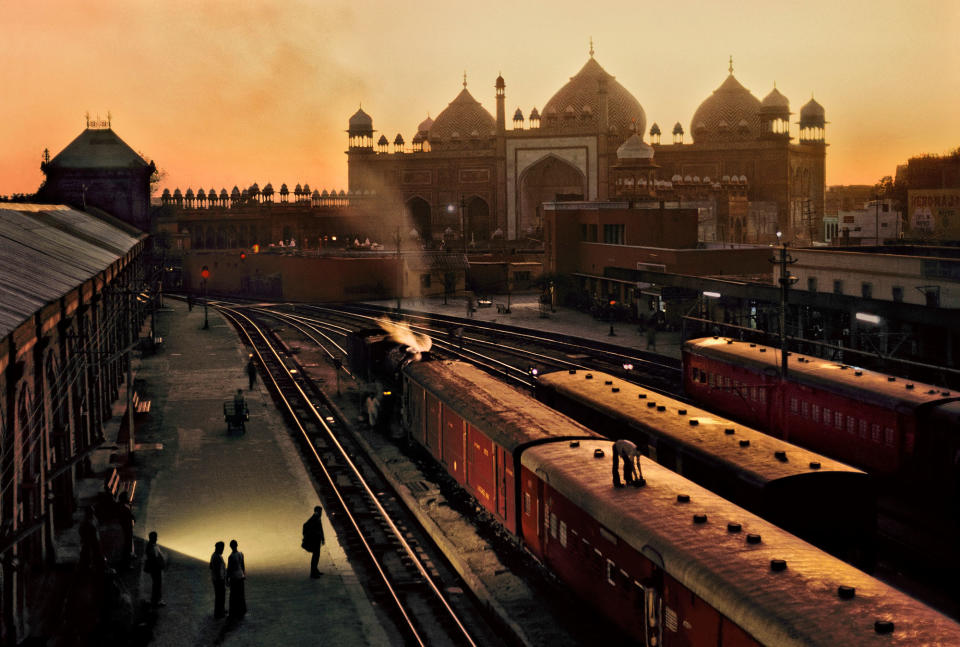 <p>Agra Fort Railway Station at dusk, with the Jama Masjid in the distance, Agra, Uttar Pradesh, India, 1983. “I photographed this image at Agra Fort Railway Station, in India, where an attendant adjusted a ventilator on the top of a train carriage. The domes and minarets of the Jama Masjid, a mosque completed in 1656 under Mughal emperor Shah Jahan, were visible in the late afternoon light.” (© Steve McCurry/Magnum Photos) </p>