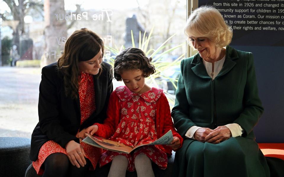 The Queen Consort listens to a young girl reading during a visit to the Coram Beanstalk charity. Next to the child is her adoptive mother - Justin Tallis/Reuters