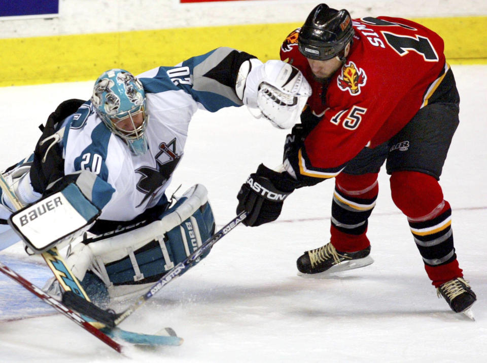 FILE -San Jose Sharks goalie Evgeni Nabokov, left, makes a save on Calgary Flames' Chris Simon during third period NHL playoff action in Calgary, Sunday, May 16, 2004. Former NHL enforcer Chris Simon has died. He was 52. Simon died Monday night, March 18, 2024, according to a spokesperson for the NHL Players' Association. (Jeff McIntosh/The Canadian Press via AP, File)