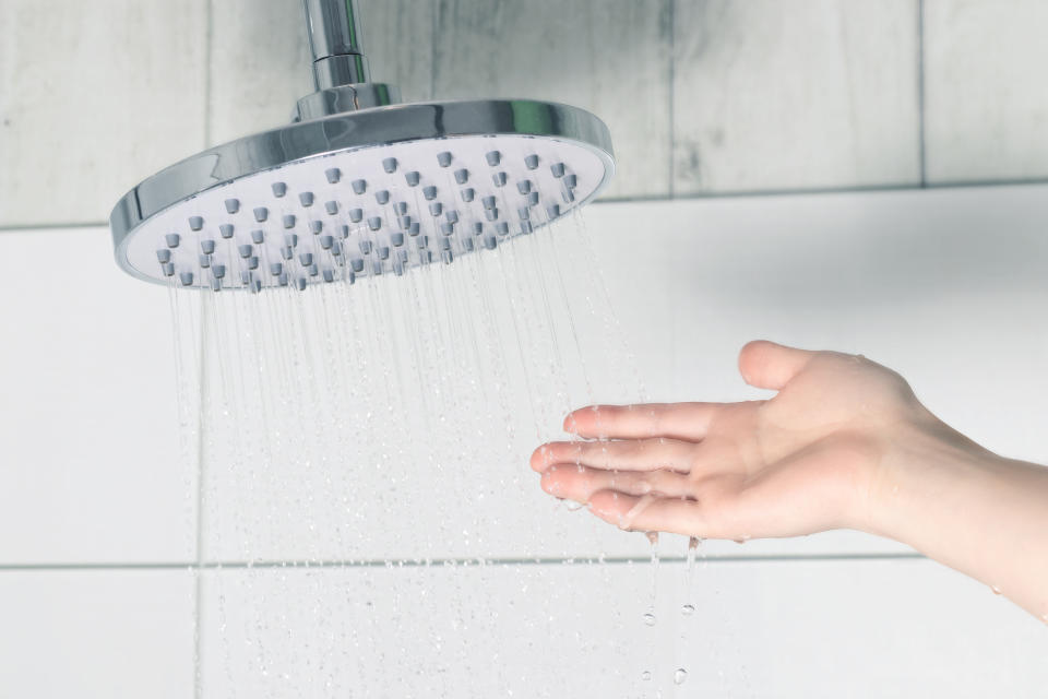 Female hand touching water pouring from a rain shower head, checking water temperature.