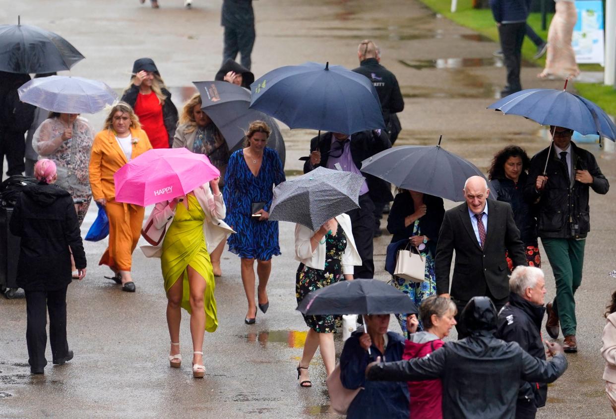 Racegoers shelter from the rain as they arrive for day five of the Qatar Goodwood Festival at Goodwood Racecourse (PA)