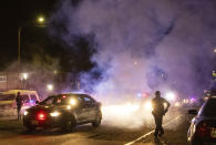 Oakland police officers walk through smoke as several hundred demonstrators confront them during a protest against police brutality in Oakland, Calif., on Friday, April 16, 2021. (AP Photo/Ethan Swope)