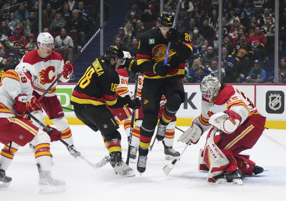 Calgary Flames goalie Jacob Markstrom (25) stops Vancouver Canucks' Jack Studnicka (18) as Dakota Joshua (81) jumps in front of him during the second period of an NHL hockey game Saturday, April 8, 2023, in Vancouver, British Columbia. (Darryl Dyck/The Canadian Press via AP)