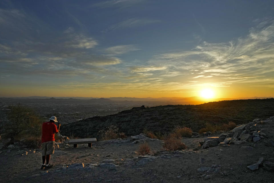 Un excursionista fotografía la salida del sol el lunes 17 de julio de 2023, sobre el valle que domina la cima de South Mountain, en Phoenix. (AP Foto/Matt York)