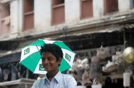 A boy holds an umbrella imprinted with national flags while selling them from a stall at a market ahead of Independence day in Karachi, Pakistan July 29, 2017. REUTERS/Akhtar Soomro