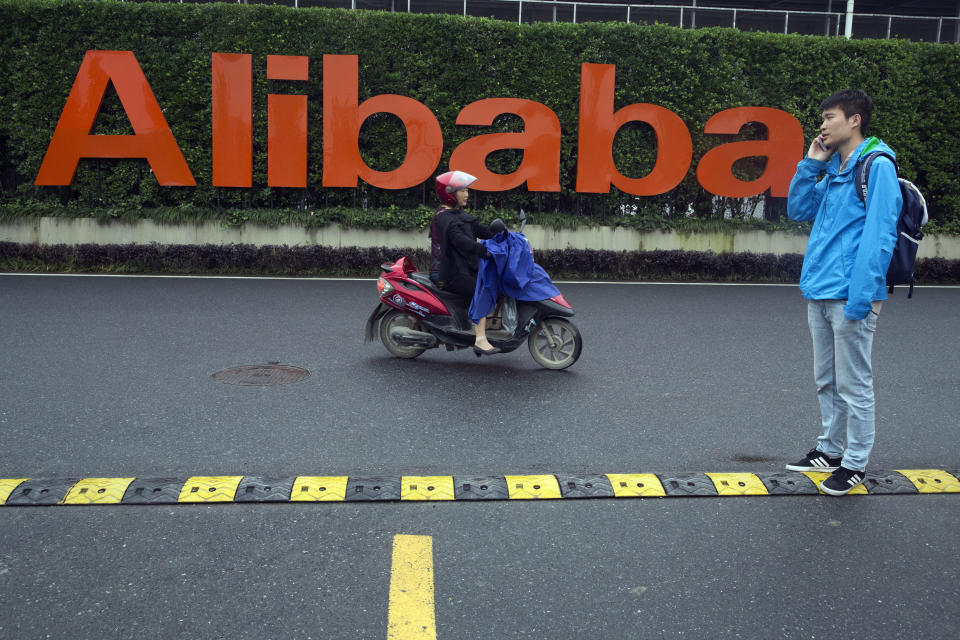 FILE - In this May 27, 2016, file photo, a man talks on his phone as a woman rides on an electric bike past a company logo at the Alibaba Group headquarters in Hangzhou in eastern China's Zhejiang province. Companies including internet giants Alibaba and Tencent were fined Wednesday, July 7, 2021, by anti-monopoly regulators in a new move to tighten control over their fast-developing industries. (AP Photo/Ng Han Guan, File)