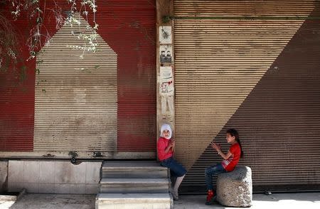 Syrian girls sit in front of shops in the rebel held besieged Douma neighbourhood of Damascus, Syria. REUTERS/Bassam Khabieh