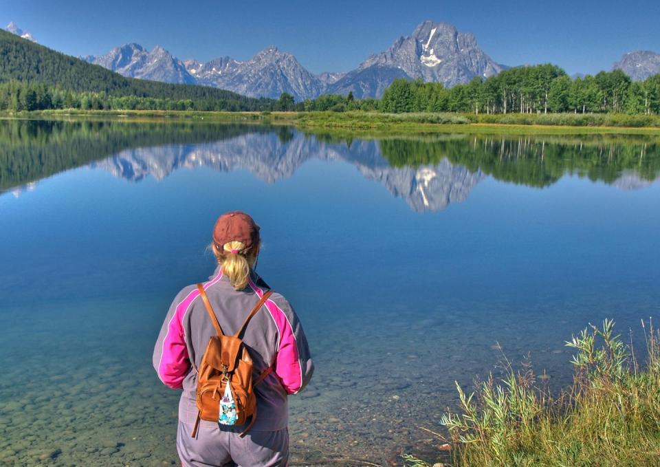 a woman stares at the reflected image of a mountain range in the still water of a river