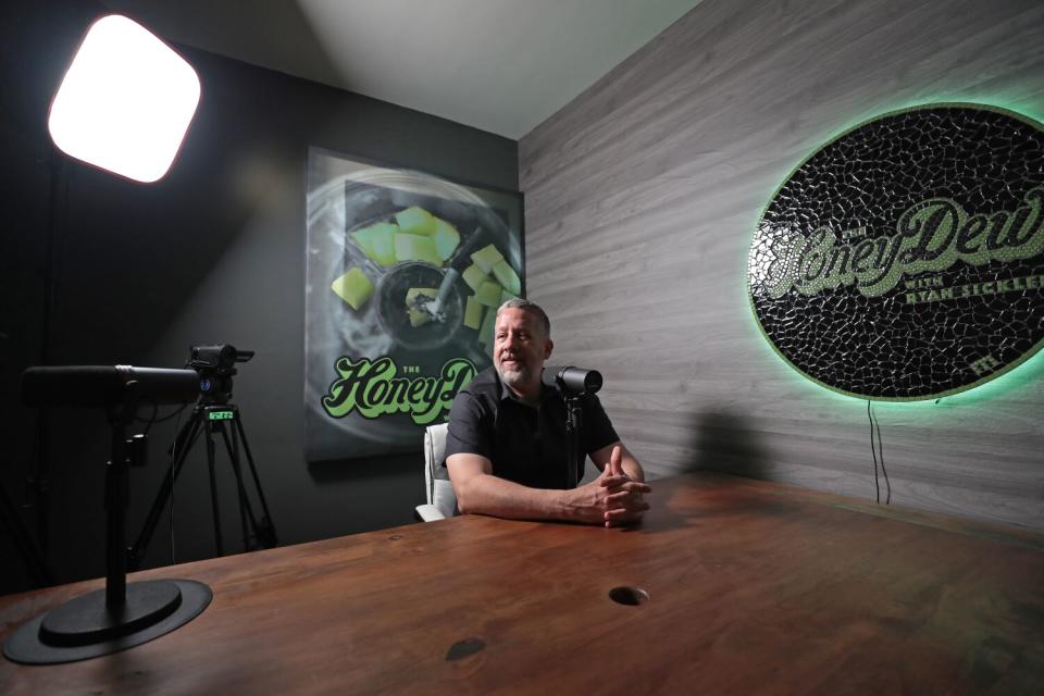 A man sitting at aa desk in front of a podcast mic