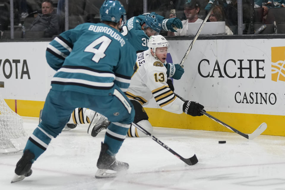 Boston Bruins center Charlie Coyle (13) reaches for the puck between San Jose Sharks defenseman Kyle Burroughs (4) and defenseman Mario Ferraro during the second period of an NHL hockey game in San Jose, Calif., Thursday, Oct. 19, 2023. (AP Photo/Jeff Chiu)