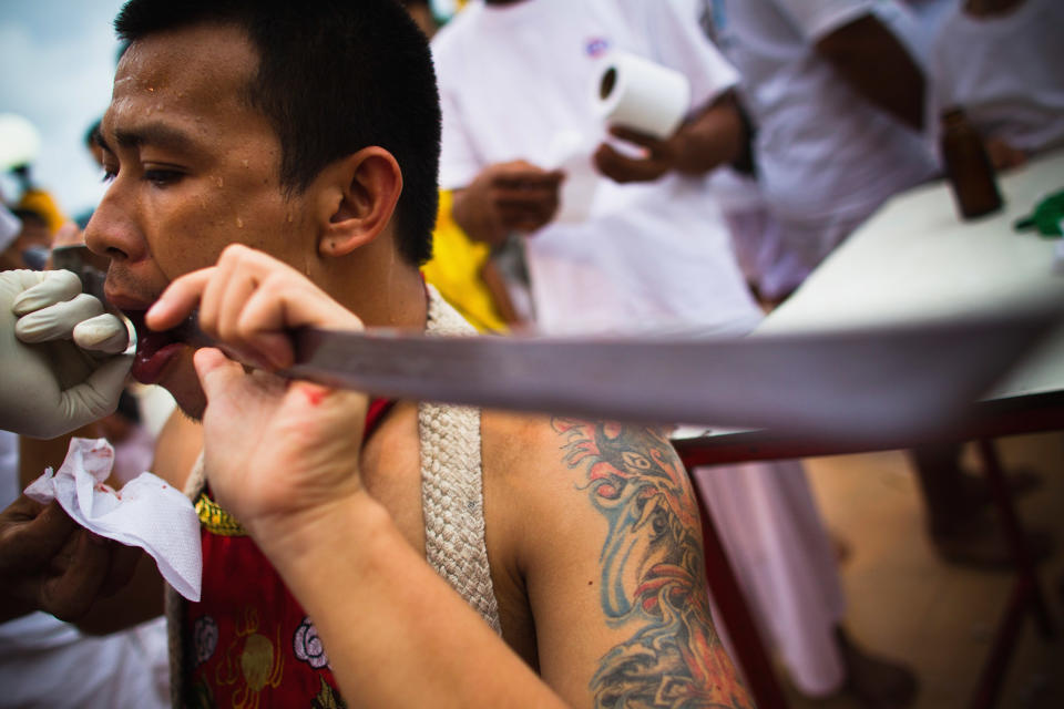 PHUKET, THAILAND - OCTOBER 05: A devotee of the Chinese shrine of Sui Boon Tong Shrine, pierces his cheeks with a sword during a procession at the Vegetarian Festival on October 5, 2011 in Phuket, Thailand. Ritual Vegetarianism in Phuket Island traces it roots back to the early 1800's. The festival begins on the first evening of the ninth lunar month and lasts for nine days. Participants in the festival perform acts of body piercing as a means of shifting evil spirits from individuals onto themselves and bring the community good luck. (Photo by Athit Perawongmetha/Getty Images)