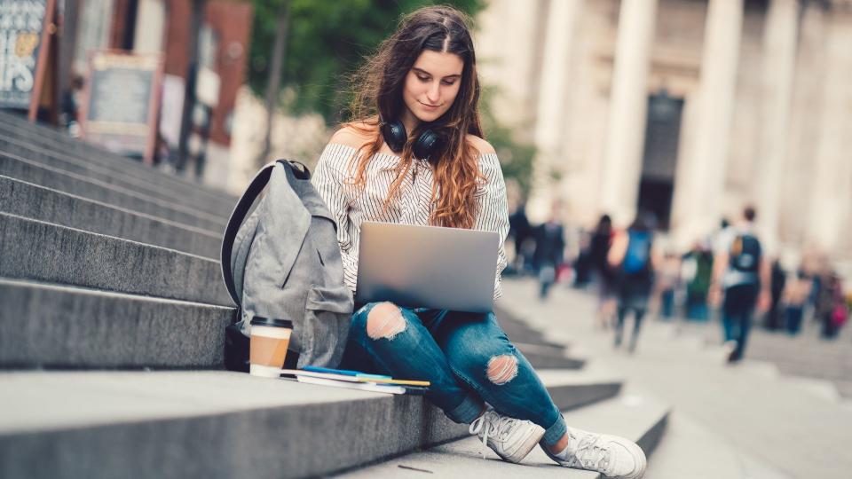 Young girl sitting at the steps and using lap top.