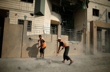 Palestinian workers clean a street outside the Ministry of Religious Affairs that was damaged by Israeli air strikes in Gaza City, July 15, 2018. REUTERS/Suhaib Salem