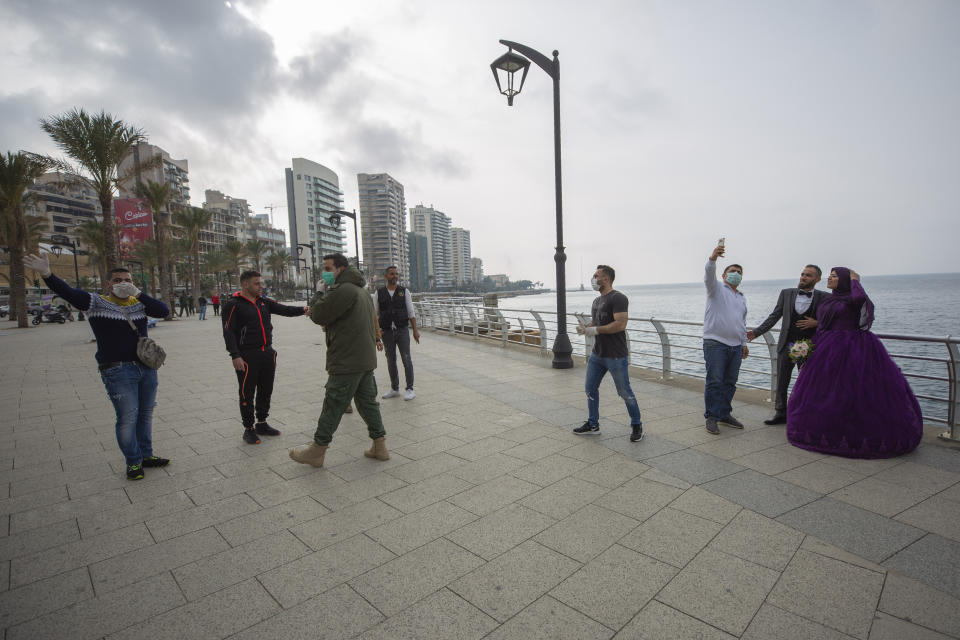 A bride and groom, right, take a selfie as Municipal policemen order them to evacuate the corniche, or waterfront promenade, along the Mediterranean Sea, as the country's top security council and the government were meeting over the spread of coronavirus, in Beirut, Lebanon, Sunday, March 15, 2020. Lebanon has been boosting precautionary measures including halting flights from several countries, closing all restaurants and nightclubs and tightening measures along the border with neighboring Syria. (AP Photo/Hassan Ammar)