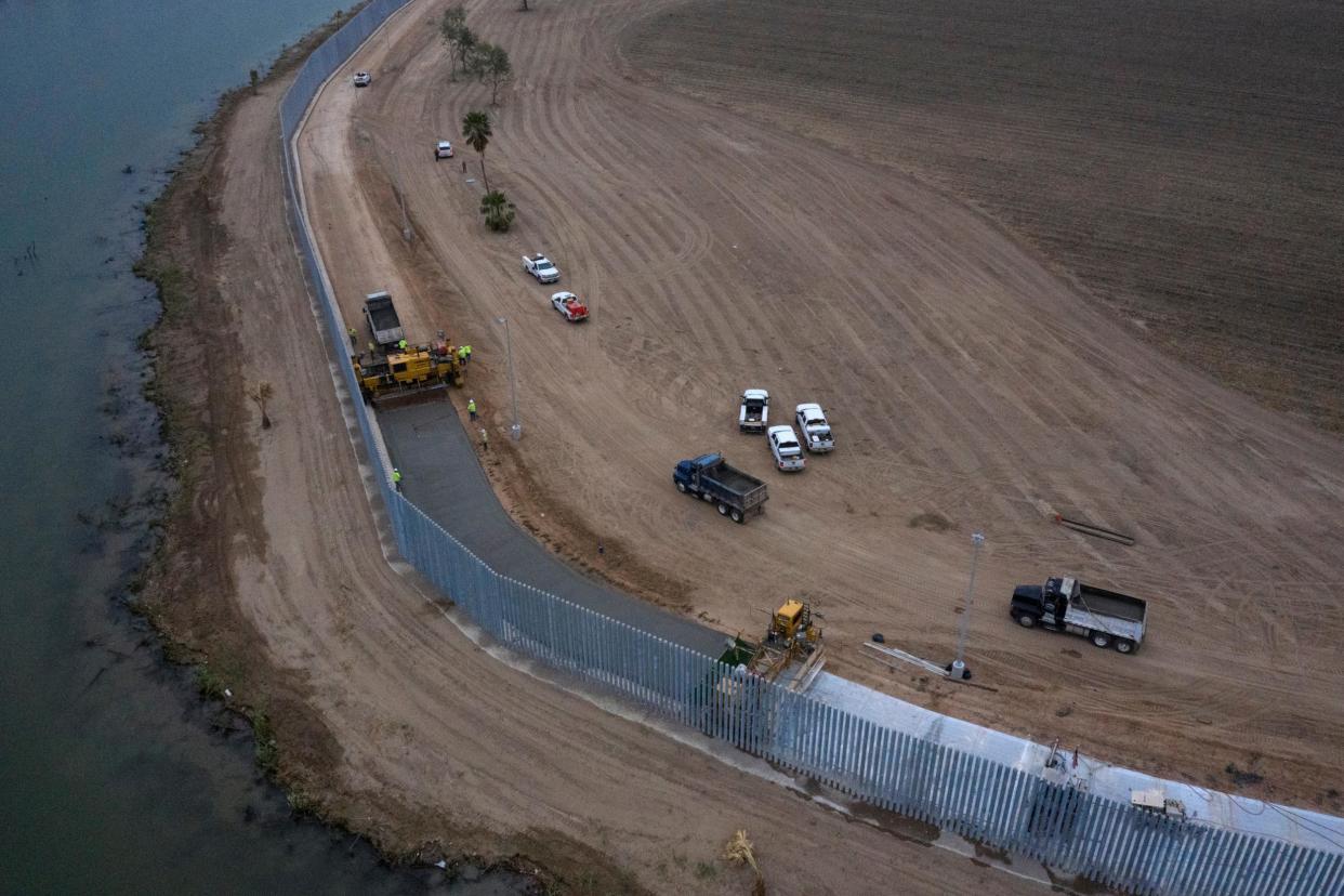 Employees of Fisher Sand & Gravel Company work near a truck as it drops concrete in front of a paving machine building a road next to a three-mile private border wall along the banks of the Rio Grande river in the town of Mission, Texas 11 on February 2020: (Reuters)