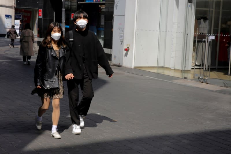 Couple, wearing masks to prevent contracting coronavirus, following outbreak of COVID-19, walk in shopping district in Seoul