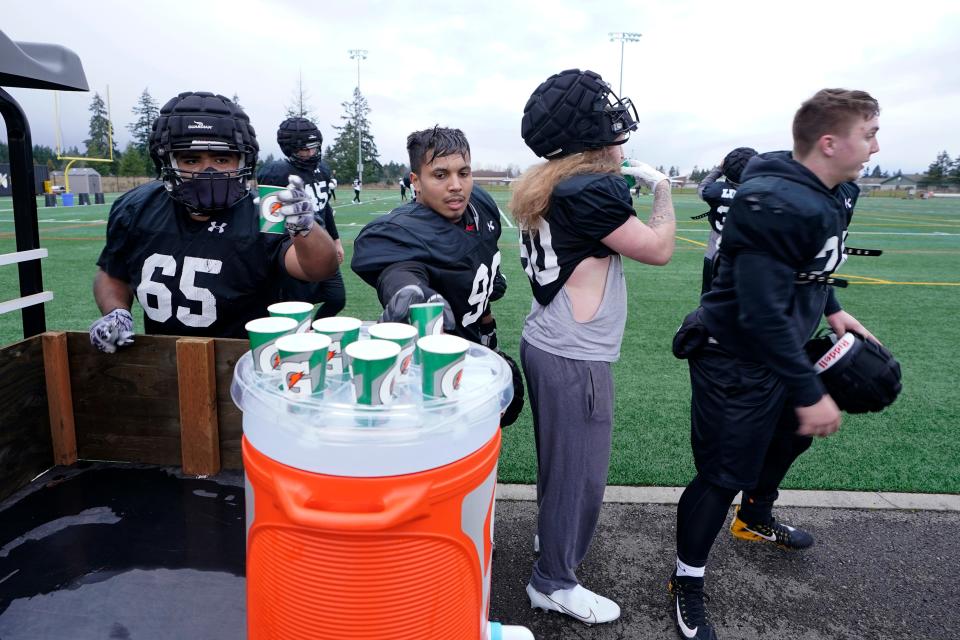 Pacific Lutheran football players help themselves to individual cups of water during a 2021 practice session.
