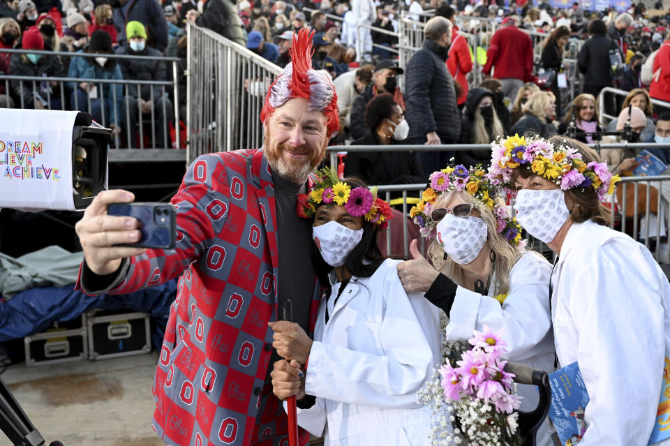 Todd Barnhart, of Ohio, takes a picture with Rose Parade volunteers Karla Thompson, Mary Townsend and Carol Convey, from left, at the 133rd Rose Parade in Pasadena, Calif., Saturday, Jan. 1, 2022. A year after New Year's Day passed without a Rose Parade due to the coronavirus pandemic, the floral spectacle celebrating the arrival of 2022 proceeded Saturday despite a new surge of infections due to the omicron variant. (AP Photo/Michael Owen Baker)