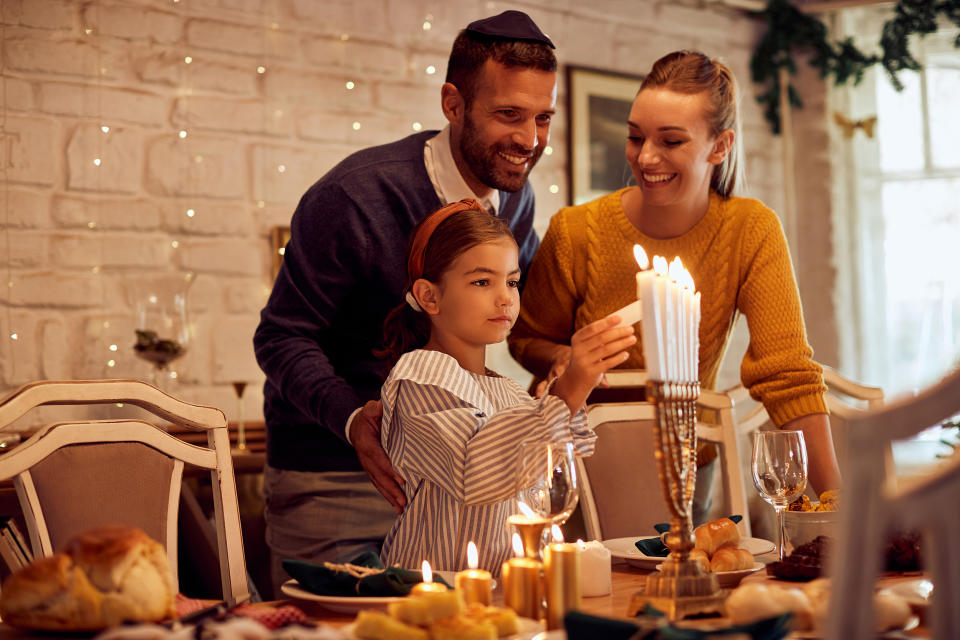 Happy Jewish family lightning the menorah before a meal at dining table. (Drazen Zigic / Getty Images stock)