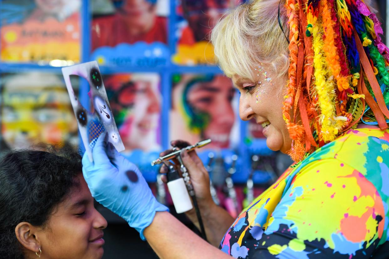 Julia Jones, with Emeralds Artistry Entertainment out of Columbia, uses a stencil to airbrush a design on Lizeth Perez, 10, in downtown Spartanburg during the Spring Fling festival on Saturday, April 29, 2023. 