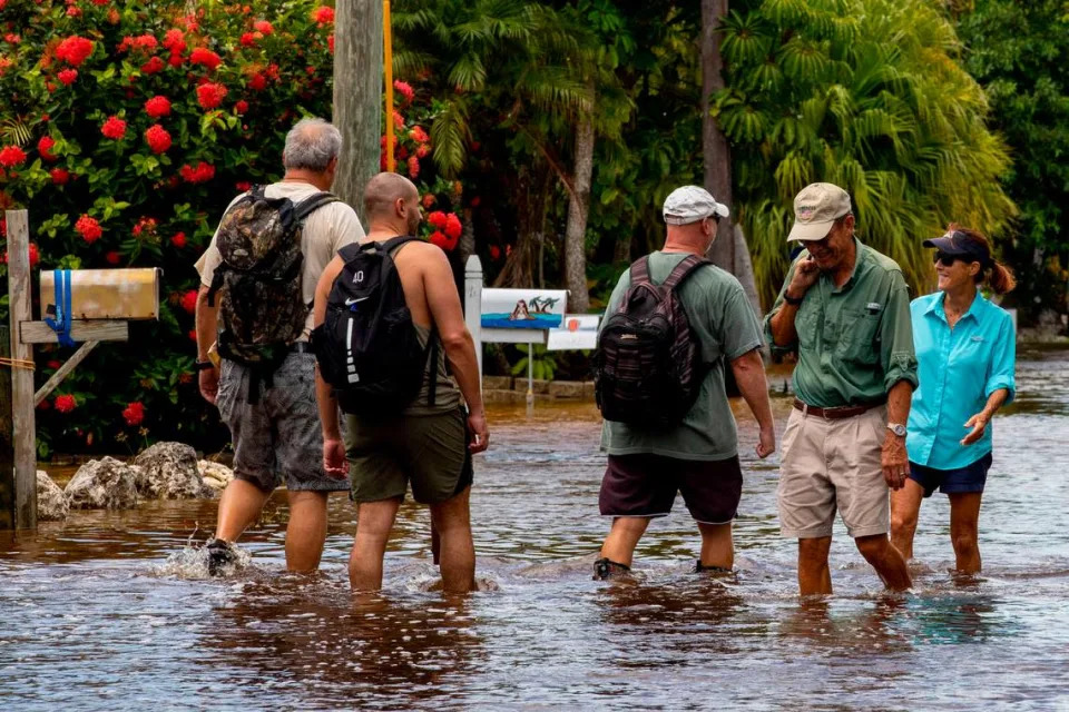 Neighbors interact as they pass one another on a wet hike up North Blackwater Lane while the street was flooded due to the effects of Hurricane Ian at Stillwright Point in Key Largo, Florida, on Thursday, September 29, 2022. Residents left their home by truck, kayak, or foot to avoid the unusually high waters.