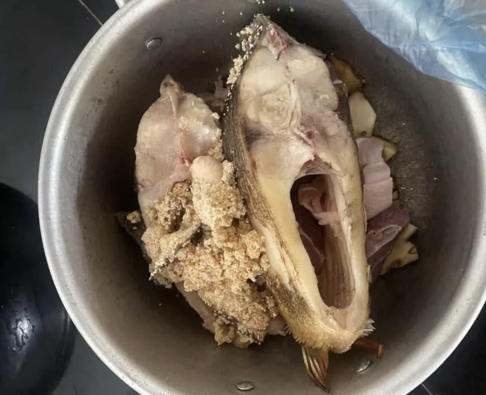 A pan full of raw fish heads and pieces, prepared for cooking.  A blue plastic bag is partially visible on the right