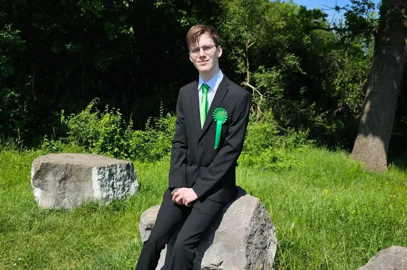Young man in black suit sat on rock in field