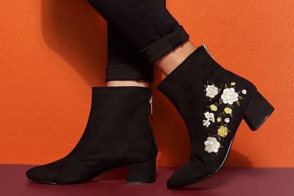 Feet sporting a pair of black cloth boots (one with flowers embroidered on the outside)