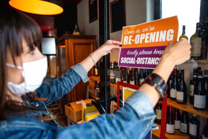 Person placing a "come in, we're re-opening" sign in their storefront after being closed because of COVID