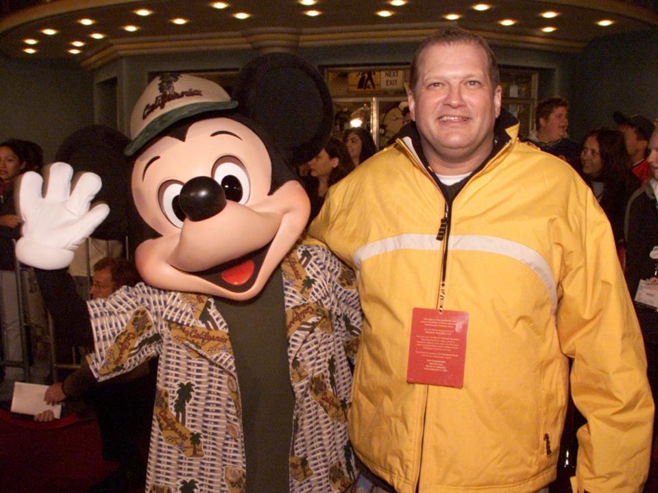 A life-size Mickey Mouse mascot waving and Drew Carey smiling.