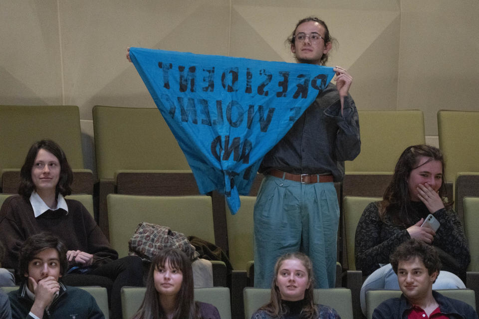 A demonstrator holds a banner as French President Emmanuel Macron explains his vision on the future of Europe during a lecture in a theatre in The Hague, Netherlands, Tuesday, April 11, 2023. (AP Photo/Peter Dejong)