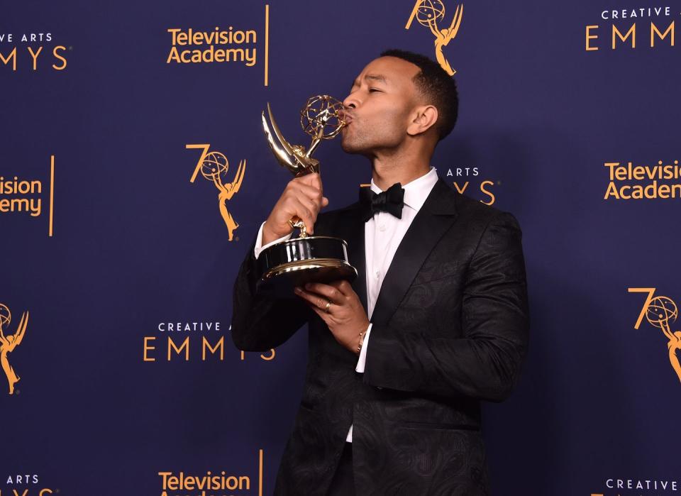 john legend, who is wearing a dark tuxedo, kisses his emmy at microsoft theater in los angeles, california