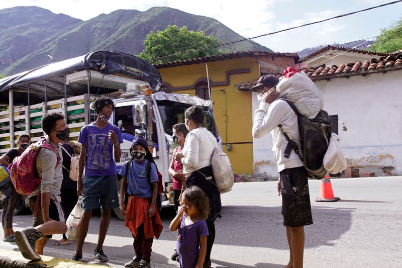 Venezuelan migrants wearing face masks hold their belongings while talking next to a Colombian highway in Pescadero