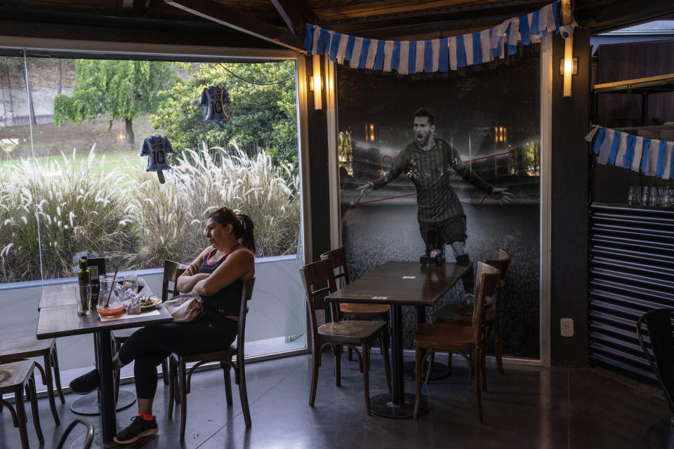 A woman eats lunch next to a picture of Lionel Messi inside a restaurant in Rosario, Argentina, Wednesday, Dec.14, 2022. (AP Photo/Rodrigo Abd)