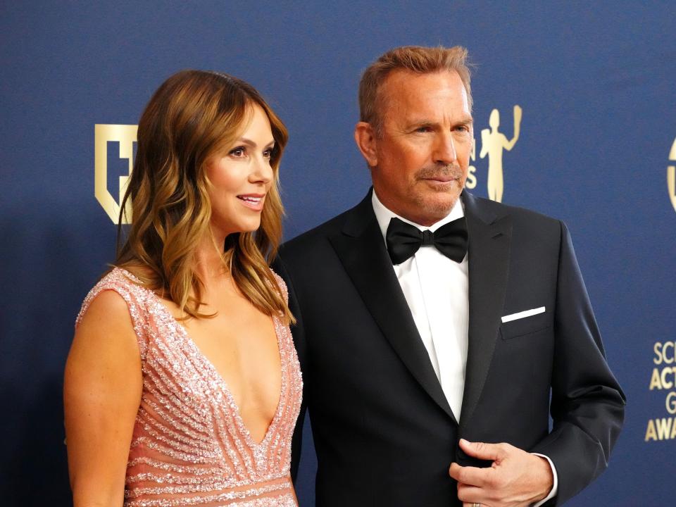 Kevin Costner and Christine Baumgartner posing together for photographers on the red carpet.