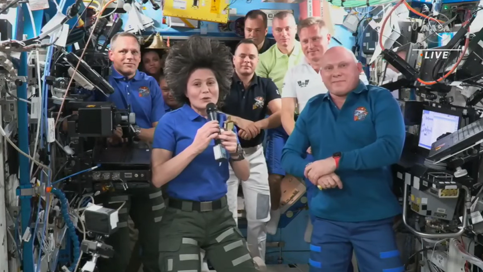 international space station astronauts cluster in a module. samantha cristoforetti is in front holding a microphone