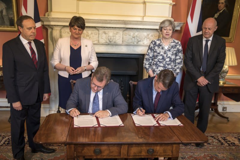 DUP議員唐納森（Jeffrey Donaldson，左坐者）與英國保守黨黨鞭威廉森（Gavin Williamson，右坐者）簽訂協議，梅伊（右二）與佛斯特（左二）站在後方觀看（AP）