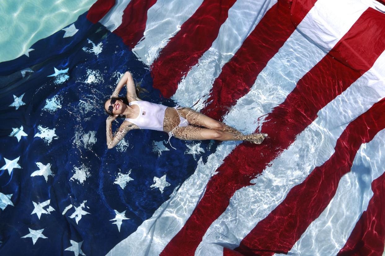 portrait of an all american girl floating in a swimming pool above american flag on a sunny day in san diego, california